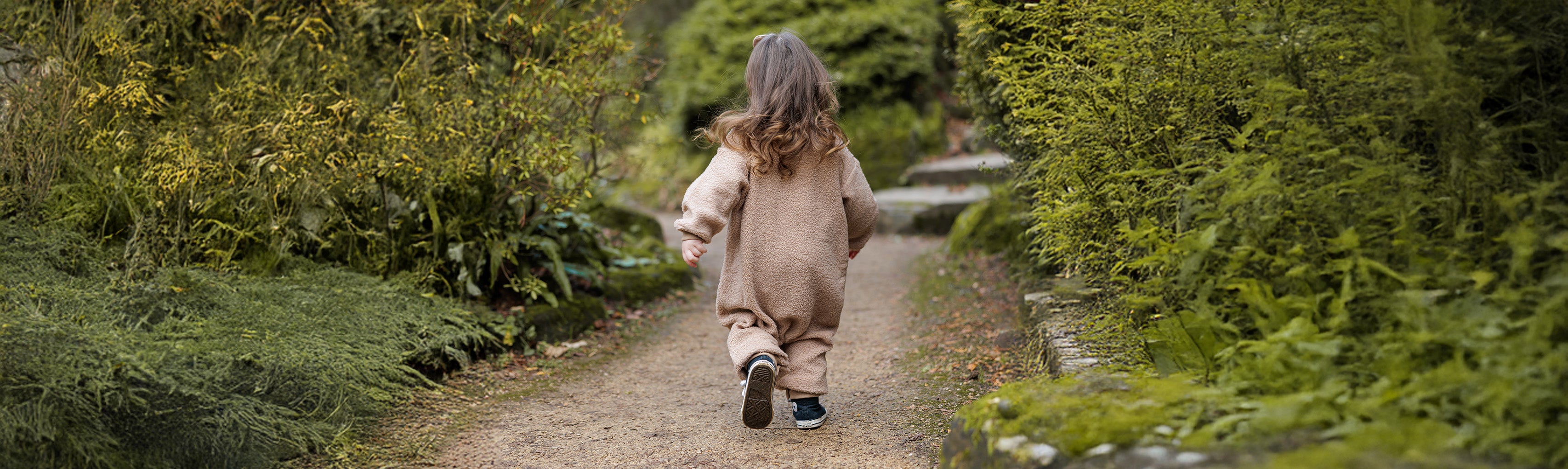 A toddler walking along a path in a garden in winter with cosy outfit on