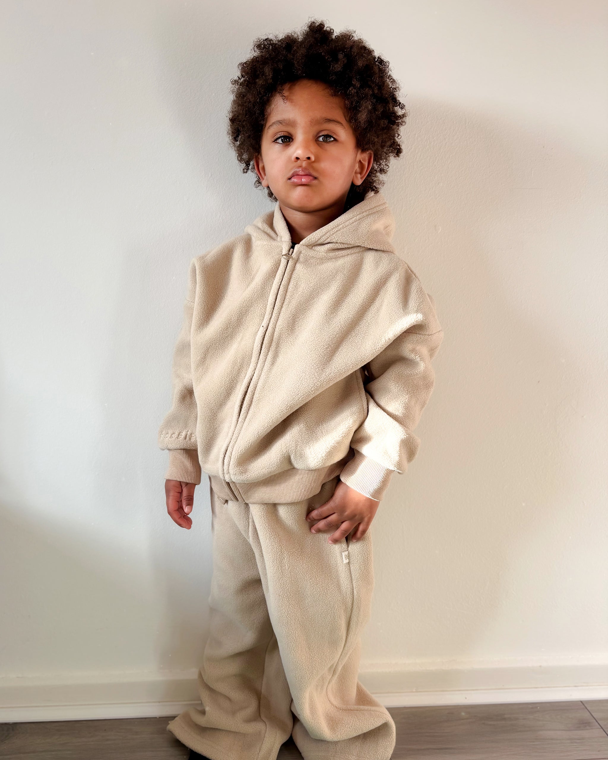 Child wearing a beige fleece tracksuit with zip up hoodie and wide leg joggers against a neutral background