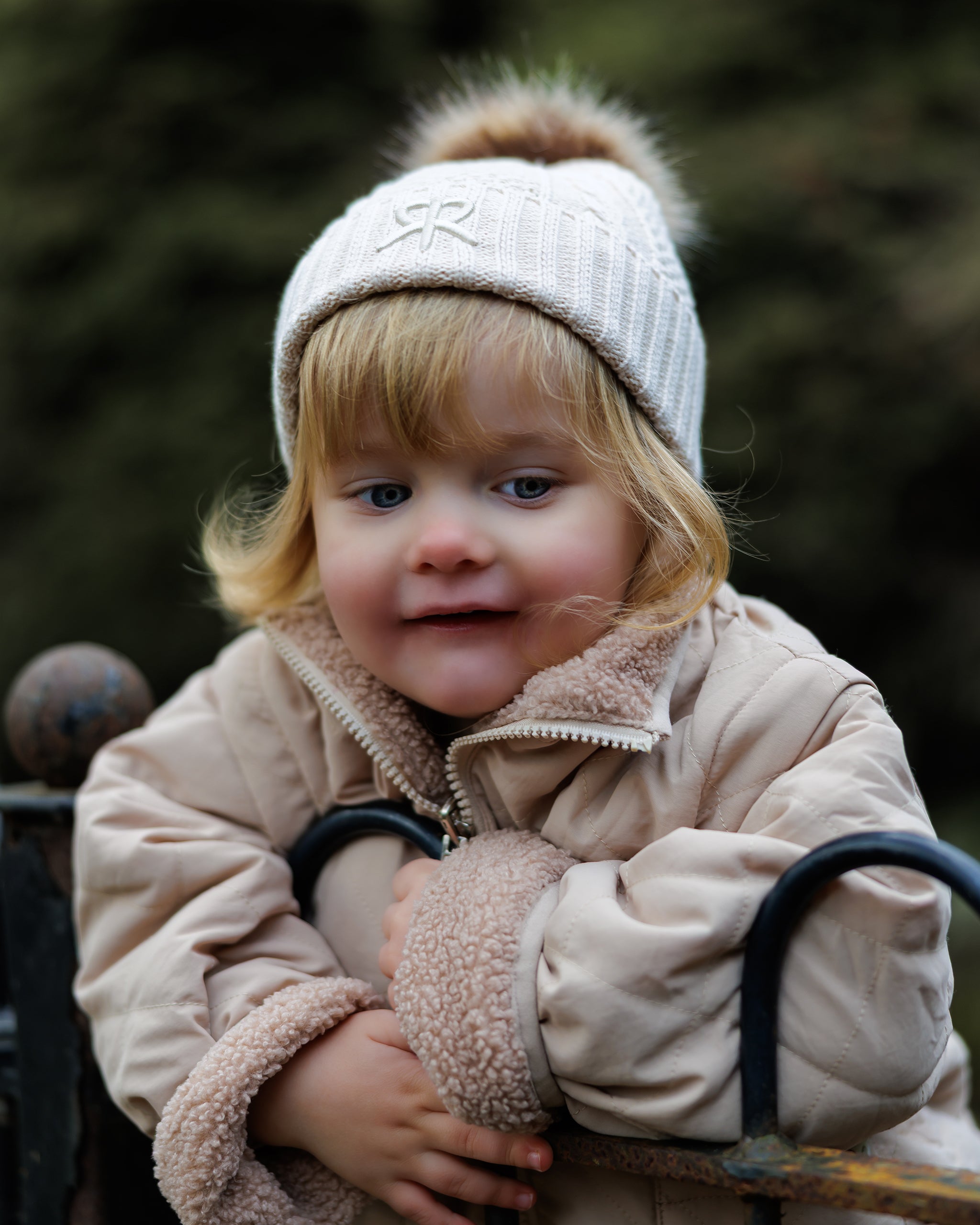 Child wearing a beige 4-in-1 reversible quilted coat and cream knit bobble beanie outdoors.