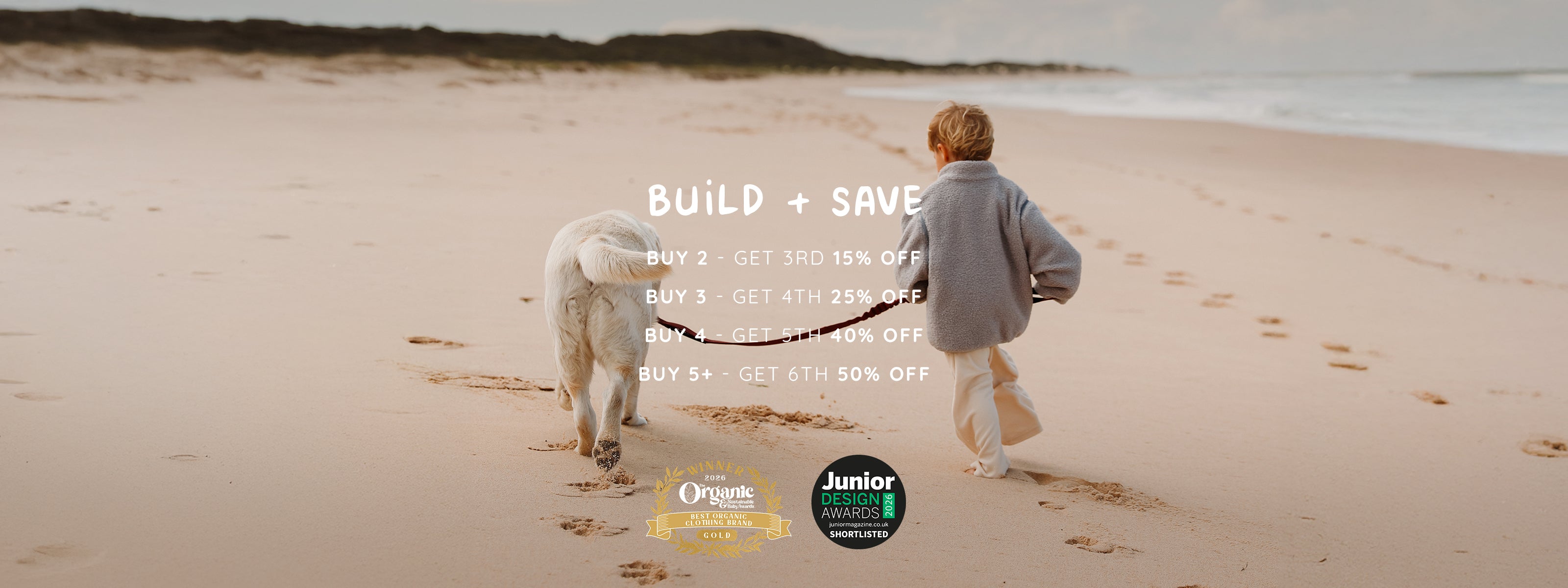 Toddler in an oversized blue (Bondi Breeze) 4-in-1 Reversible Teddy Coat and cream (Macadamia Milk) Fleece Wide Leg Joggers walking a dog on the beach