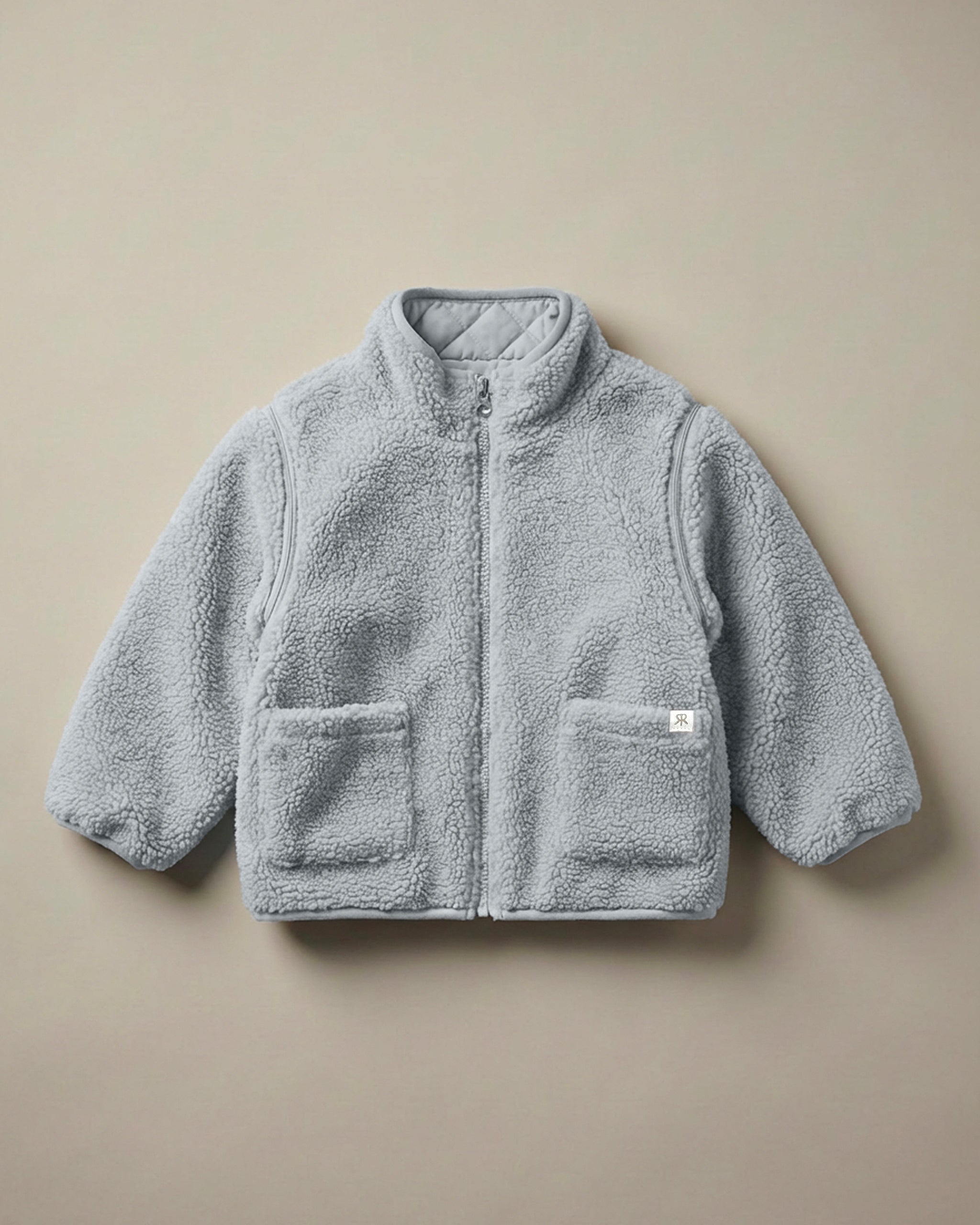 A neutral bllue-gray 4-in-1 reversible teddy fleece and quilted jacket with a soft, textured quilted fleece lining, displayed flat against a solid beige background.