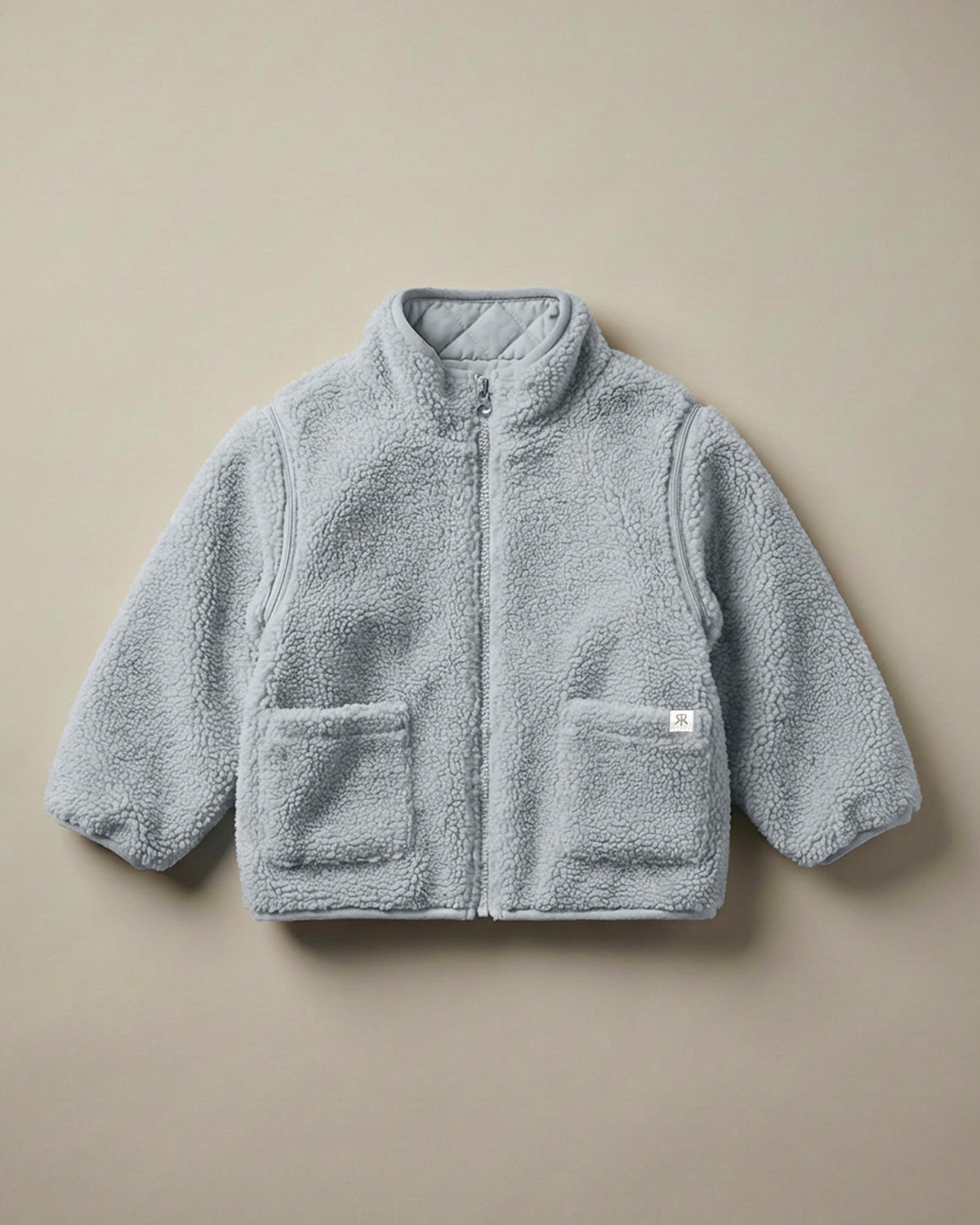 A light gray-blue teddy fleece reversible zip-up coat with a stand-up collar and two front patch pockets, laid flat against a solid beige background.