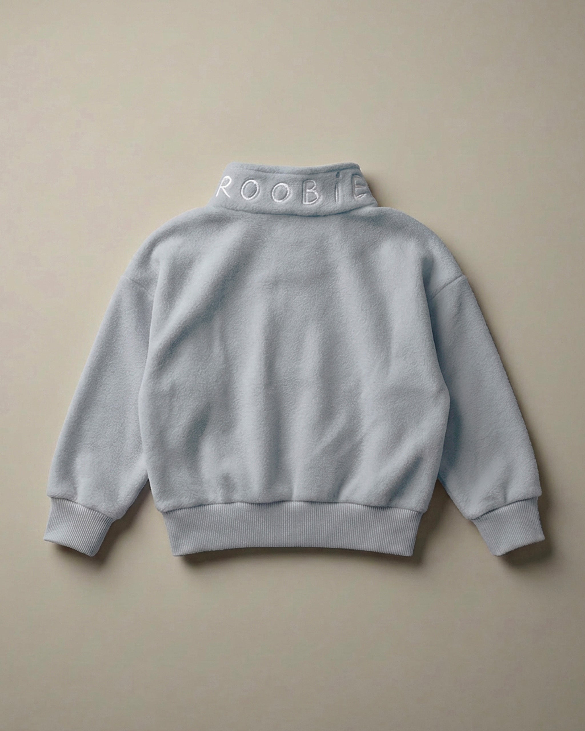 A light blue ROOBiE oversized quarter-zip sweatshirt showing the quarter-zip neckline and oversized fit in a clean product image.
