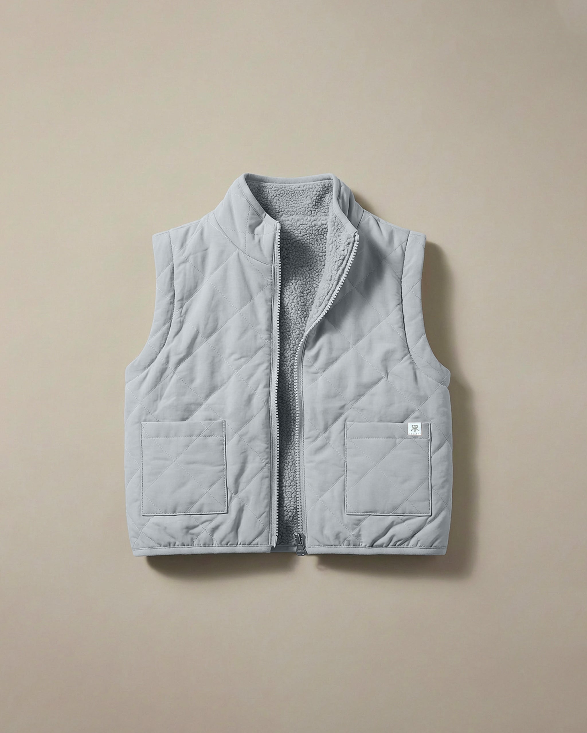 A light gray-blue quilted puffer vest with a soft teddy fleece lining, shown flat against a solid beige background.