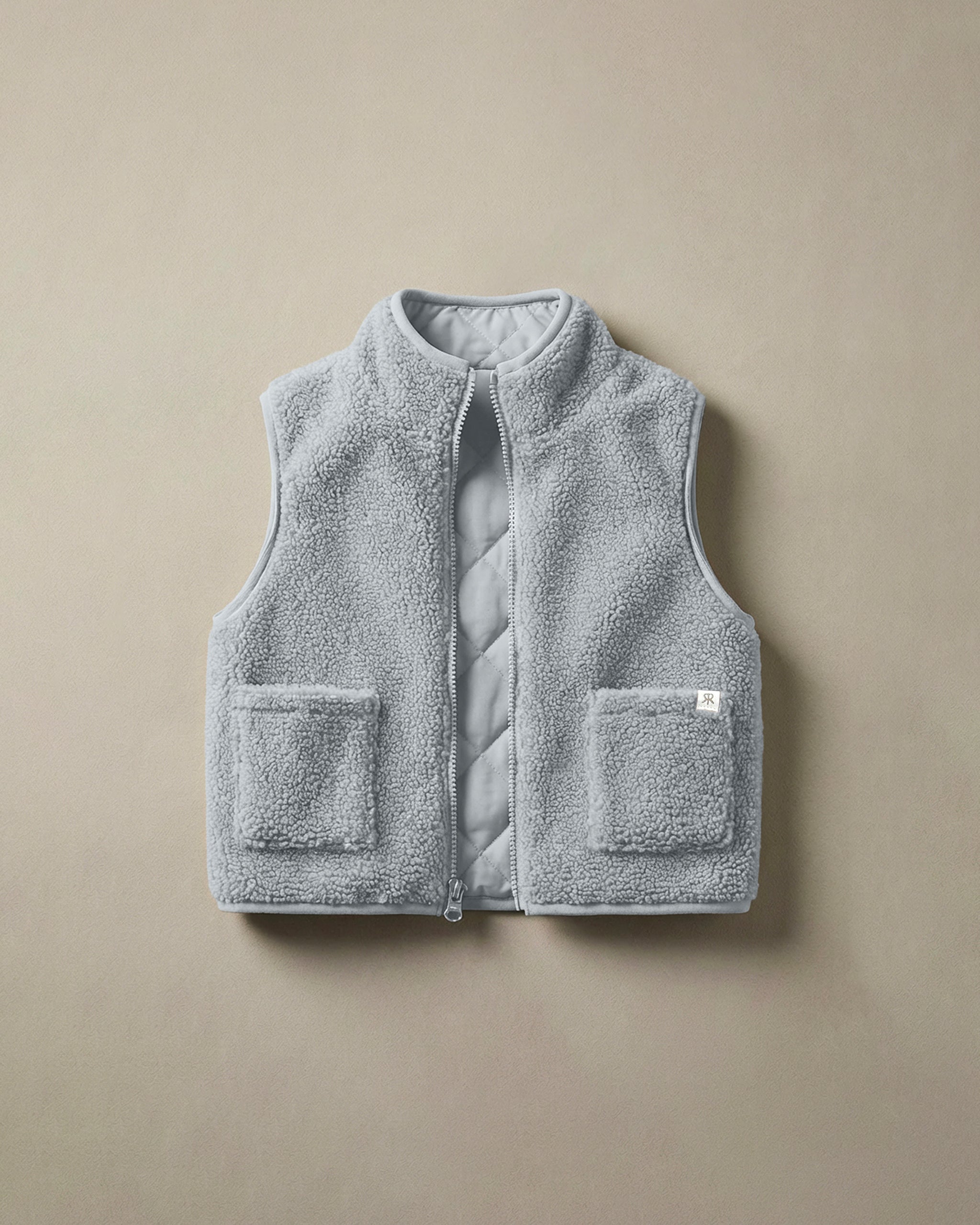 A light gray-blue teddy fleece gilet with a quilted inside panel and two front patch pockets, laid flat on a neutral beige background.