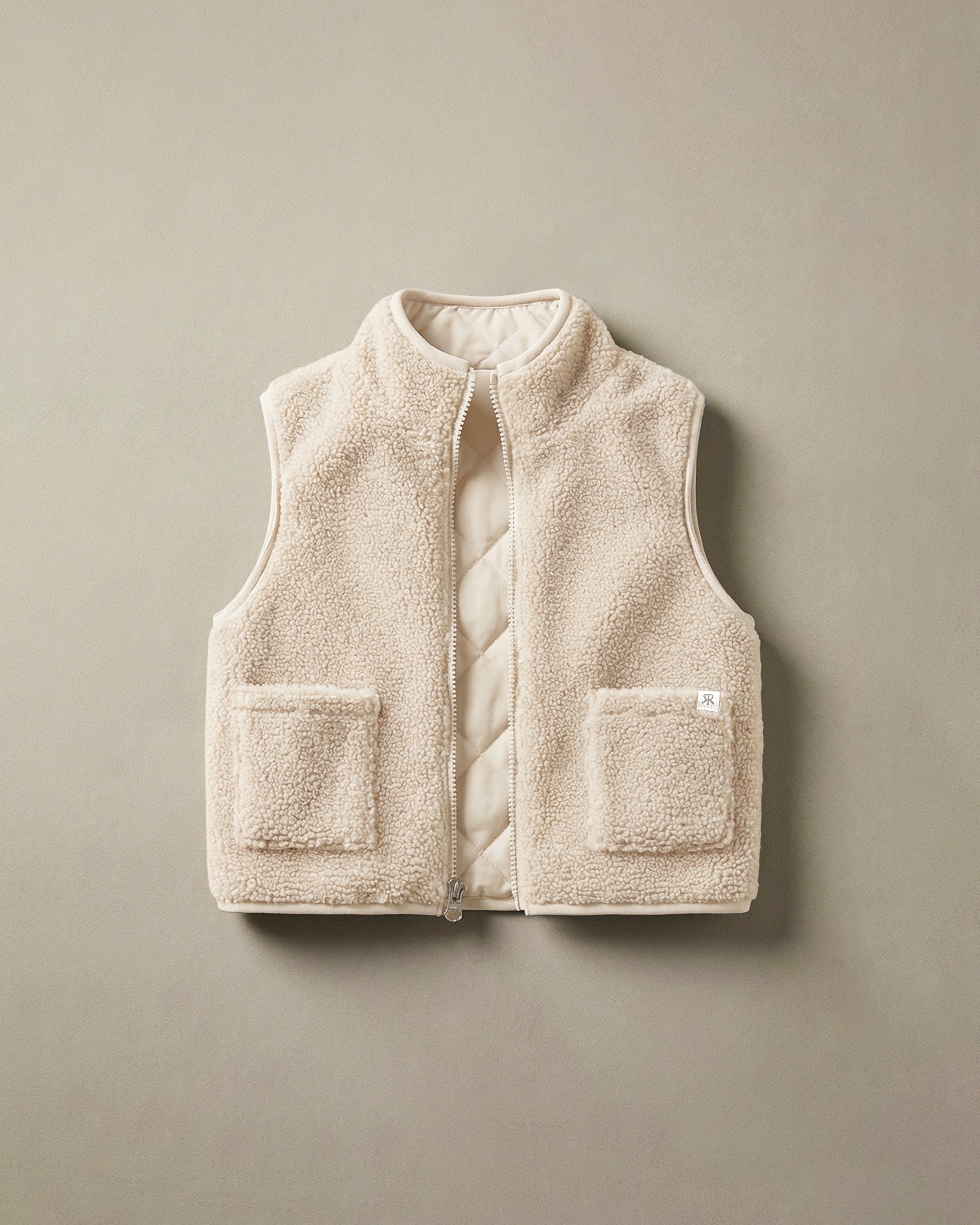 A cream-colored teddy fleece gilet with a quilted inner and two front patch pockets, displayed flat against a neutral taupe background.
