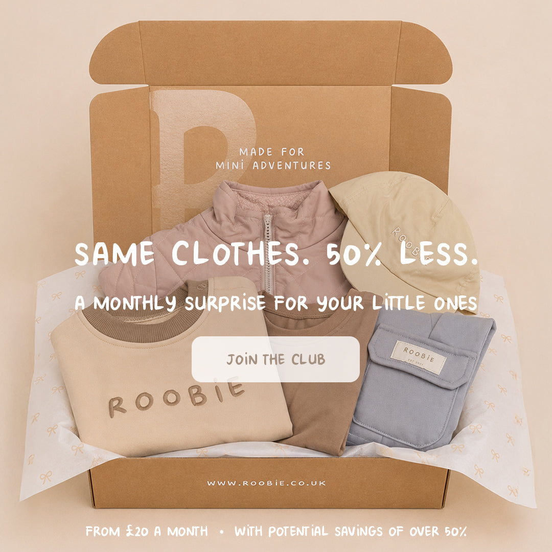 Open ROOBiE box showing a folded capsule wardrobe: quilted jacket, embroidered ROOBiE sweatshirt, joggers, cargo pants and a bucket hat in neutral tones.