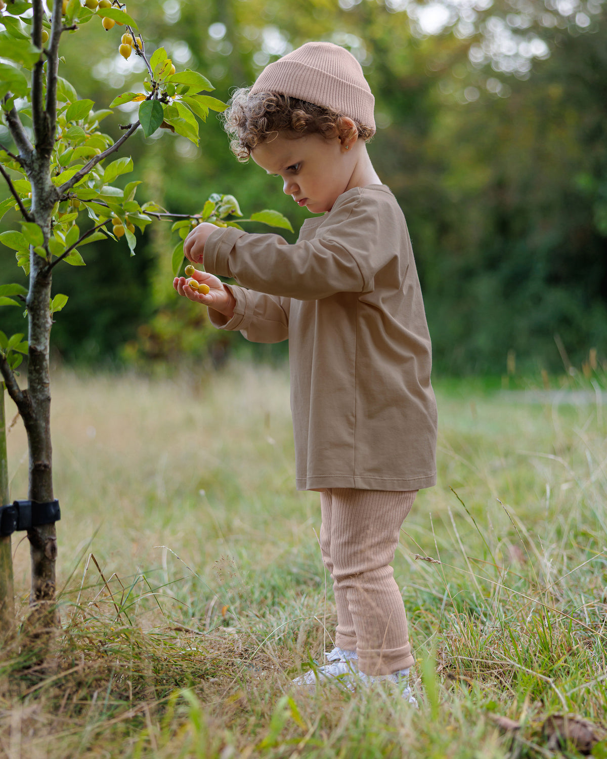 Toddler girl wearing ROOBiE long sleeve T-shirt in warm brown, with oversized fit and simple crew neckline, ribbed pink leggings and matching cotton beanie