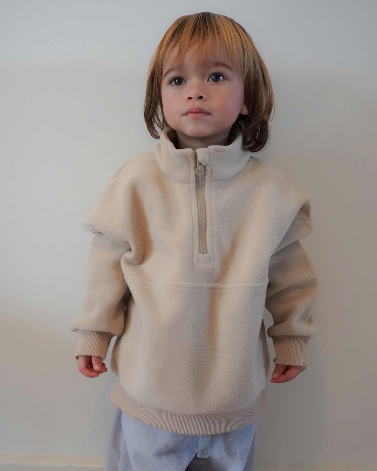 Child wearing a beige fleece quarter zip jumper against a plain background