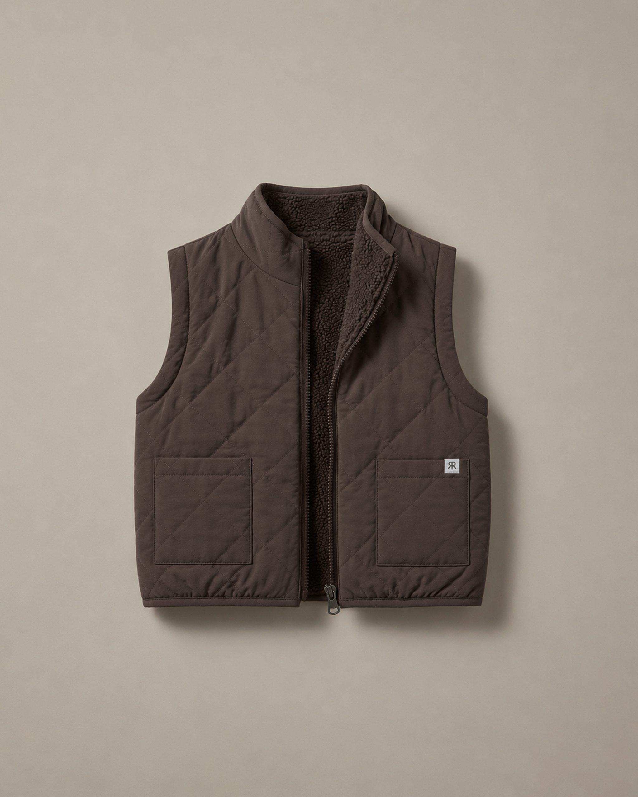 A dark brown quilted puffer vest with a soft teddy fleece lining, shown flat against a neutral beige background.