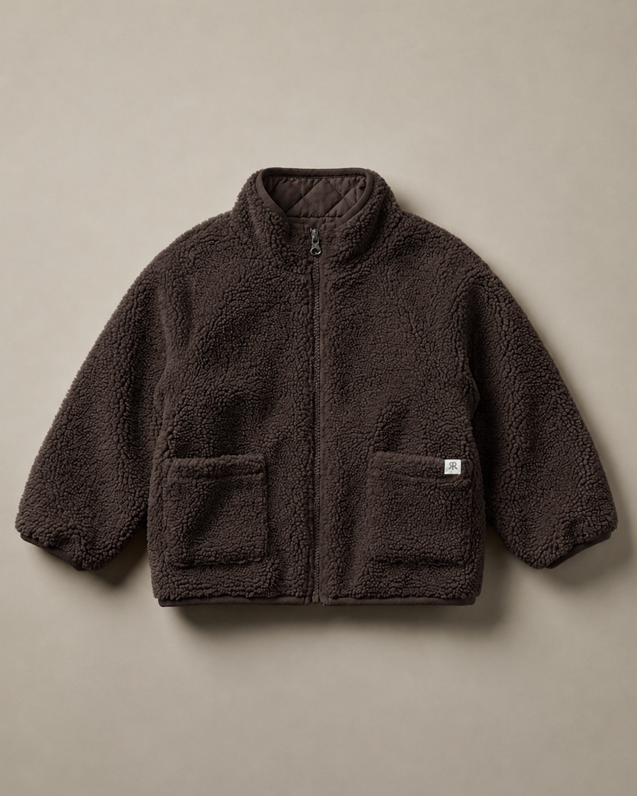 A dark brown teddy fleece zip-up jacket with a stand-up collar and two front patch pockets, laid flat against a solid taupe background.