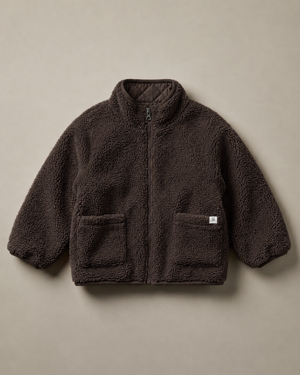 A dark brown teddy fleece zip-up jacket with a stand-up collar and two front patch pockets, laid flat against a solid taupe background.