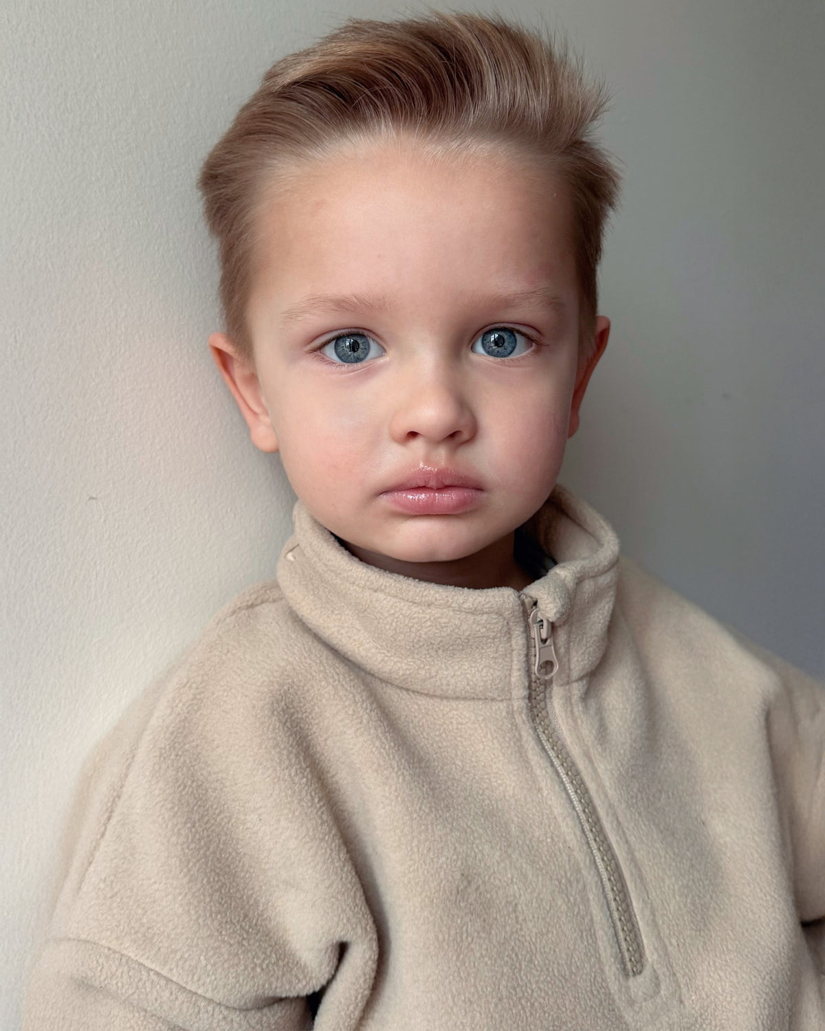 Young child wearing a beige quarter zip fleece jumper against a plain background