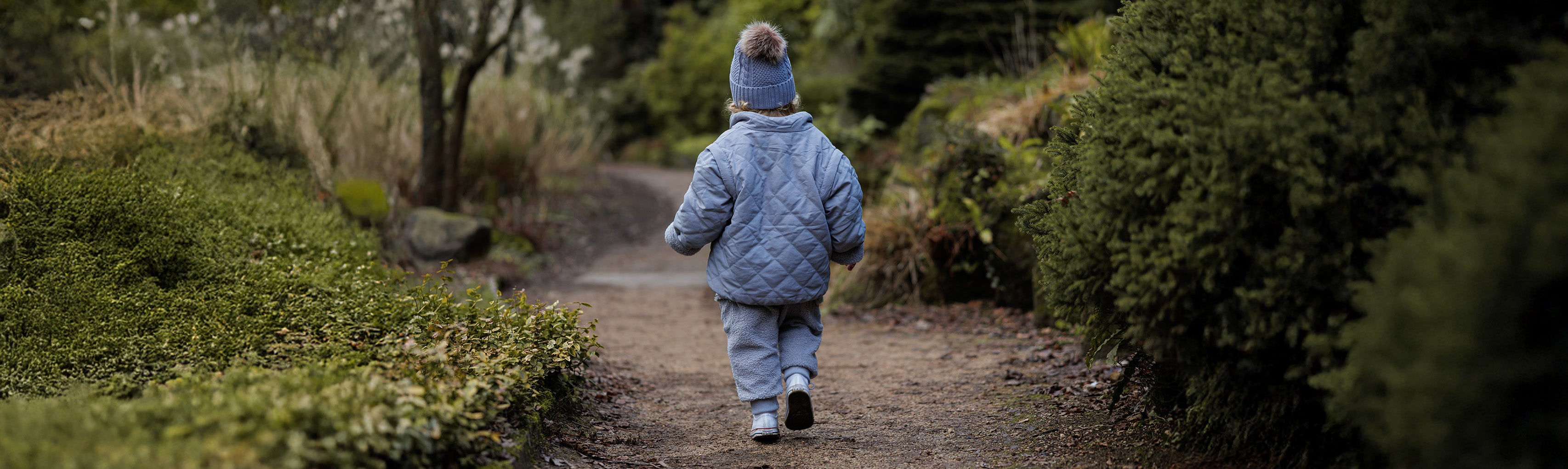 Child in a warm, cosy, reversible teddy coat walking away on a path in a winter forest