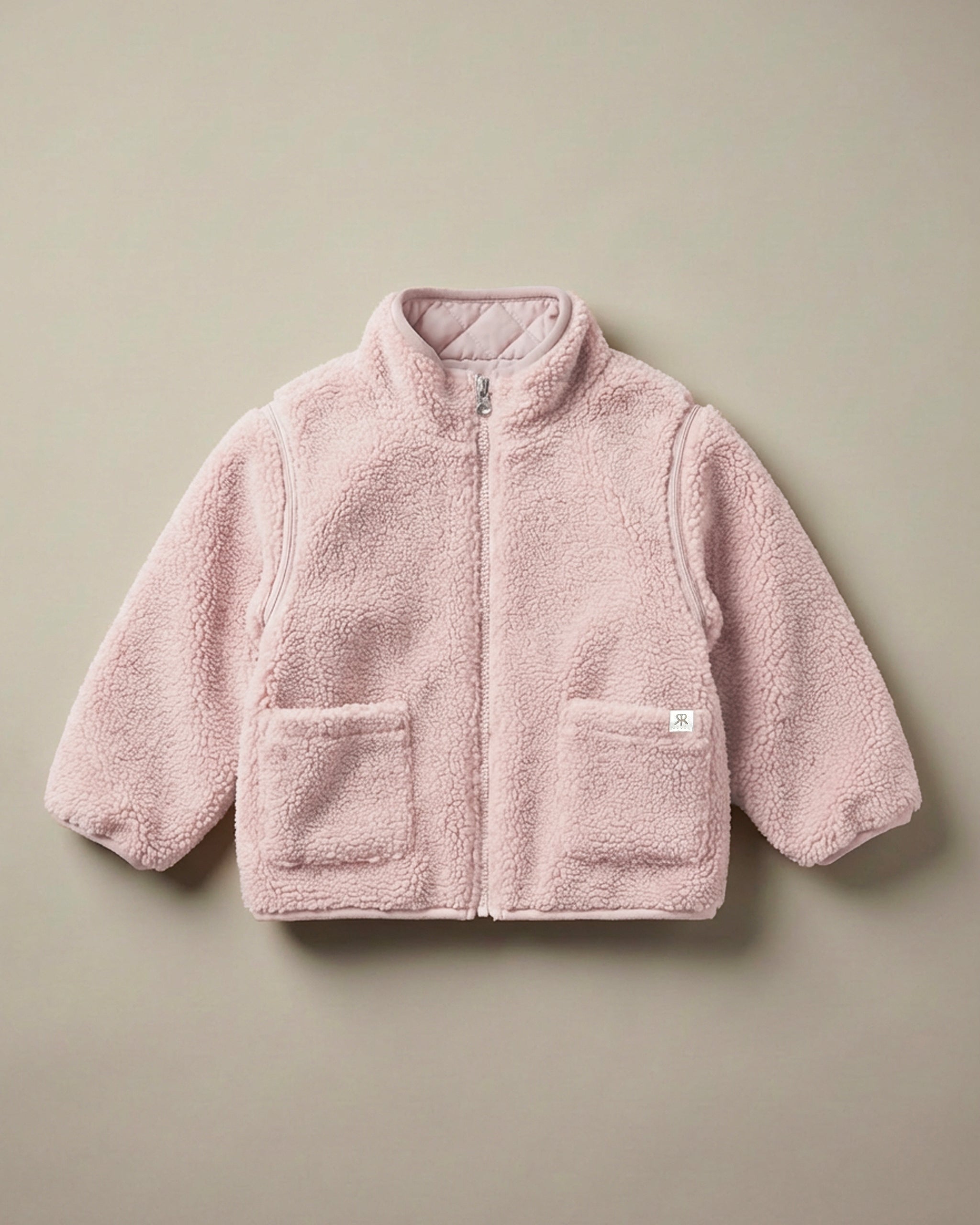 A neutral pink 4-in-1 reversible teddy fleece jacket with a soft, textured matching quilted lining, displayed flat against a solid beige background.