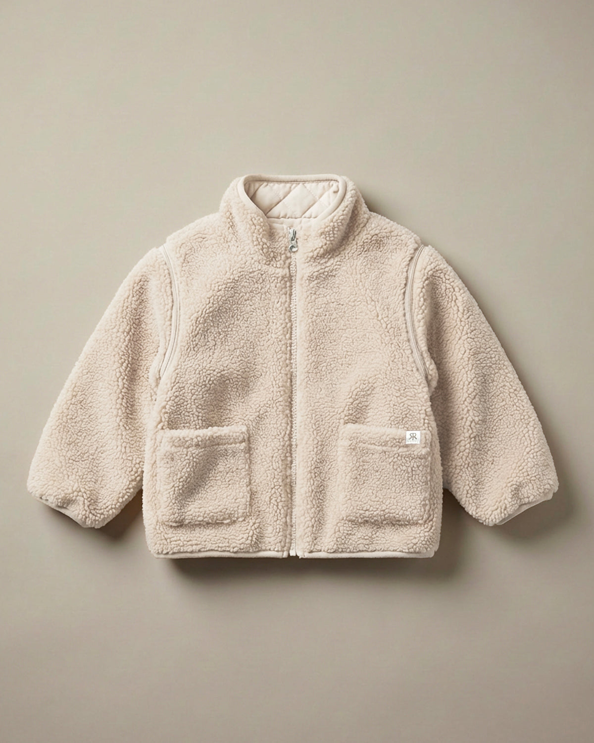 A light cream-beige teddy fleece zip-up jacket with a stand-up collar and two front patch pockets, laid flat against a solid taupe background.
