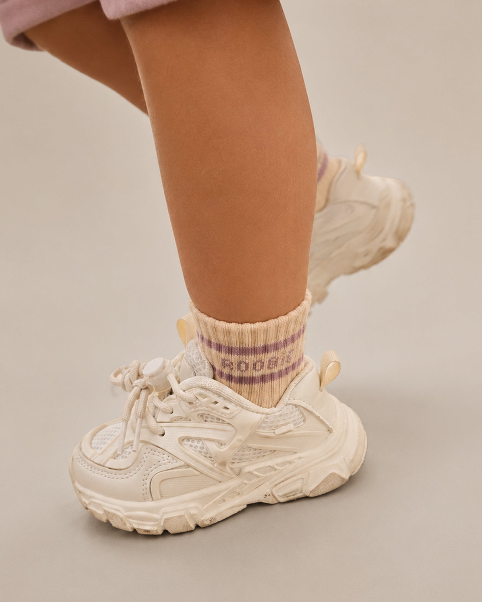 Close up of toddler wearing ROOBiE cream and pink crew socks with stripe with chunky white trainers in a neutral studio setting