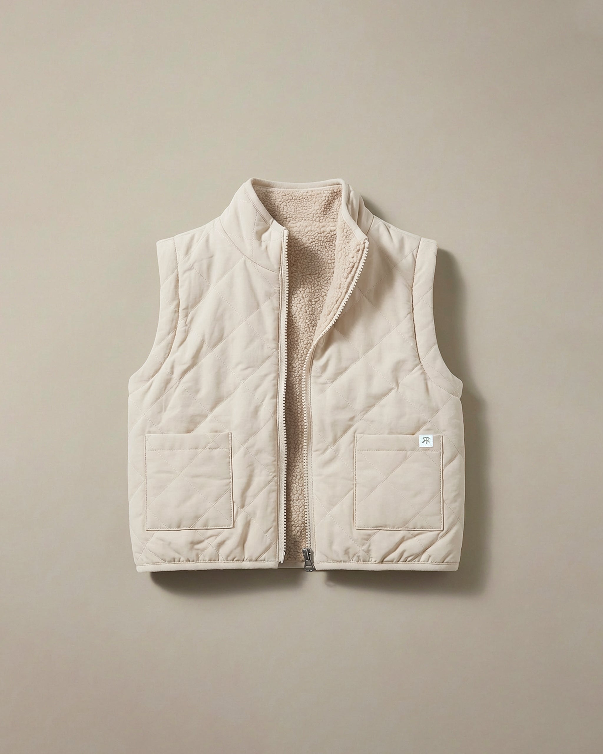 A light beige quilted puffer vest with a soft teddy fleece lining, shown flat against a neutral beige background.
