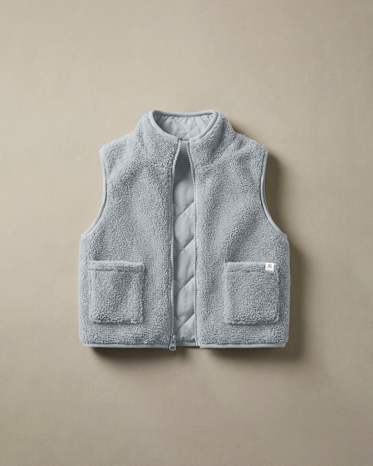 A light gray-blue teddy fleece gilet with a quilted inside panel and two front patch pockets, laid flat on a neutral beige background.
