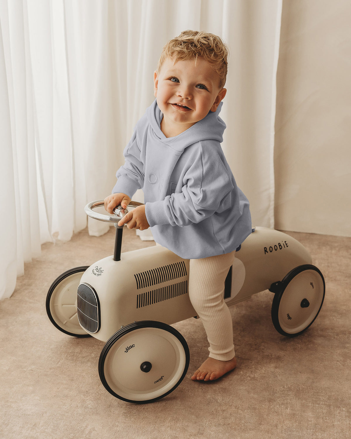 A toddler boy wearing light blue hoodie from ROOBiE, featuring oversized fit and hooded neckline, photographed against a neutral studio background.