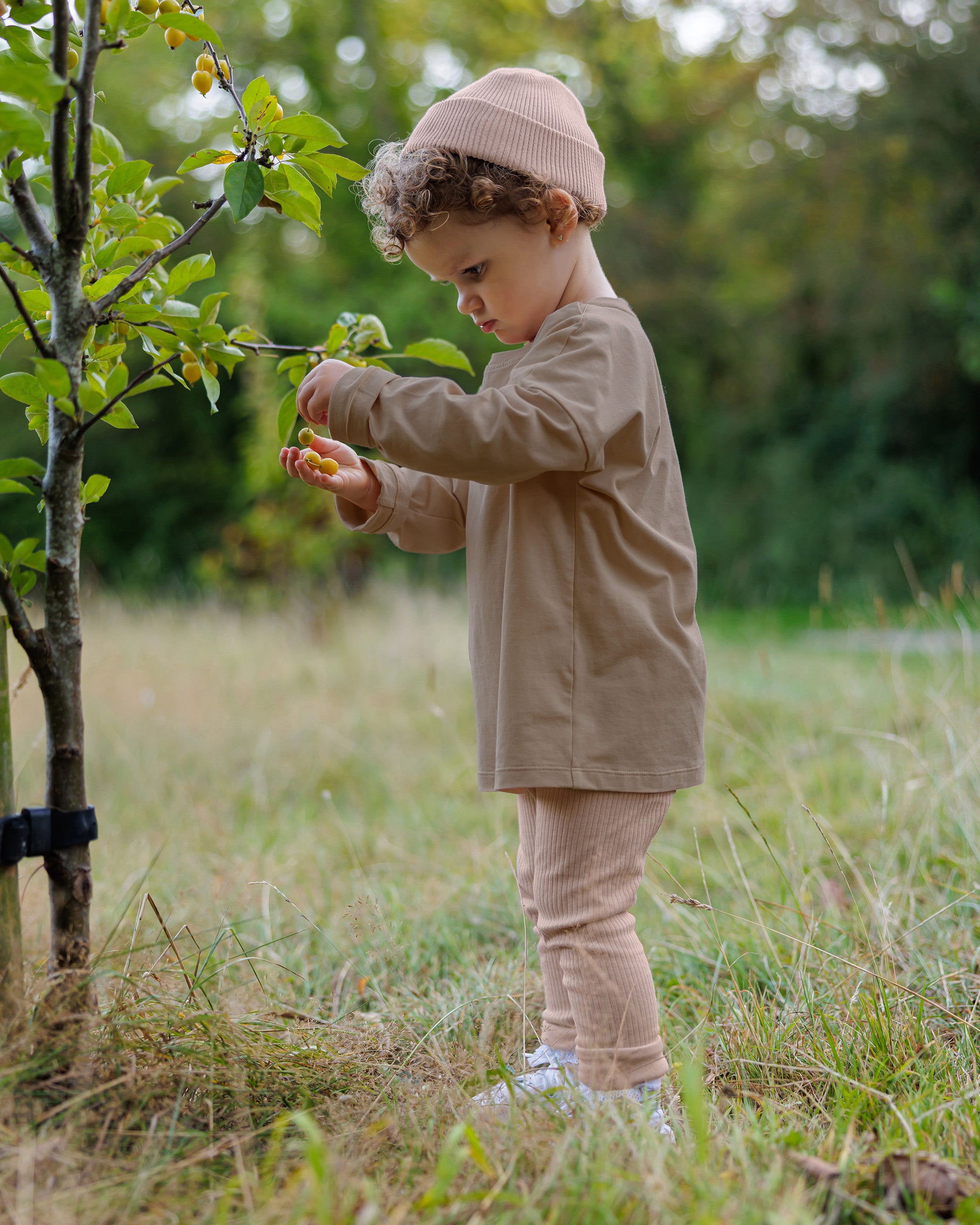 Toddler girl wearing ROOBiE long sleeve T-shirt in warm brown, with oversized fit and simple crew neckline, ribbed pink leggings and matching cotton beanie