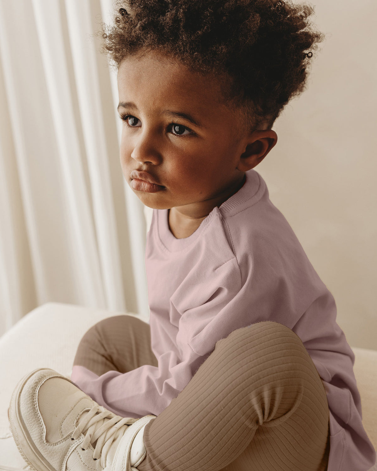 A toddler boy wearing a soft pink ROOBiE oversized long sleeve t-shirt and oversized fit in a neutral studio setting.