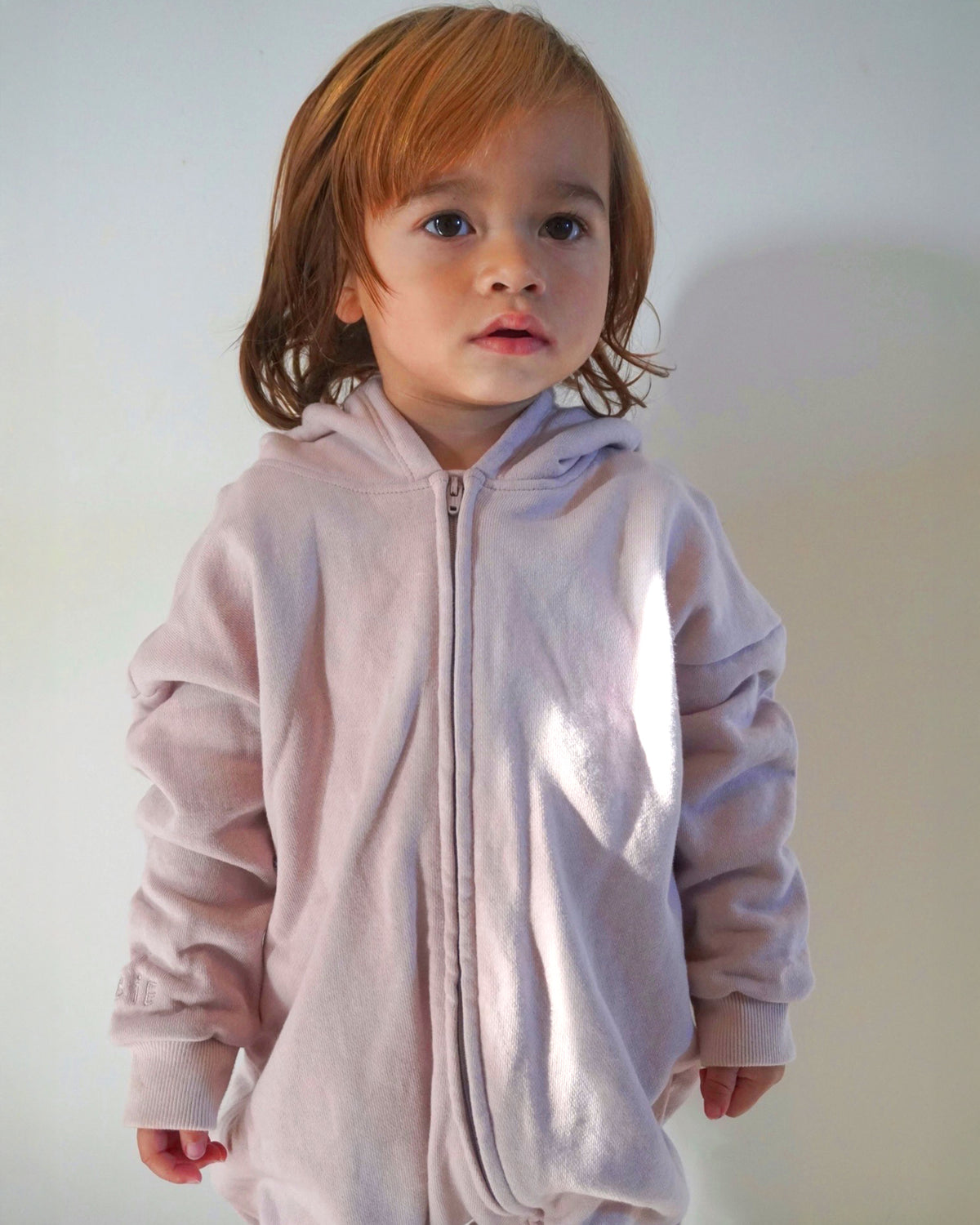 Child wearing a light pink hooded one-piece against a plain background