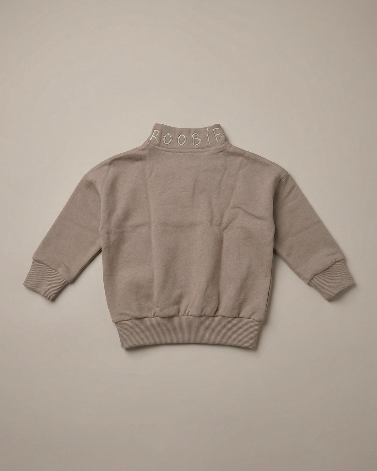 A warm brown ROOBiE quarter-zip sweatshirt showing the branded 'ROOBiE' neckline and oversized fit in a clean neutral product image.