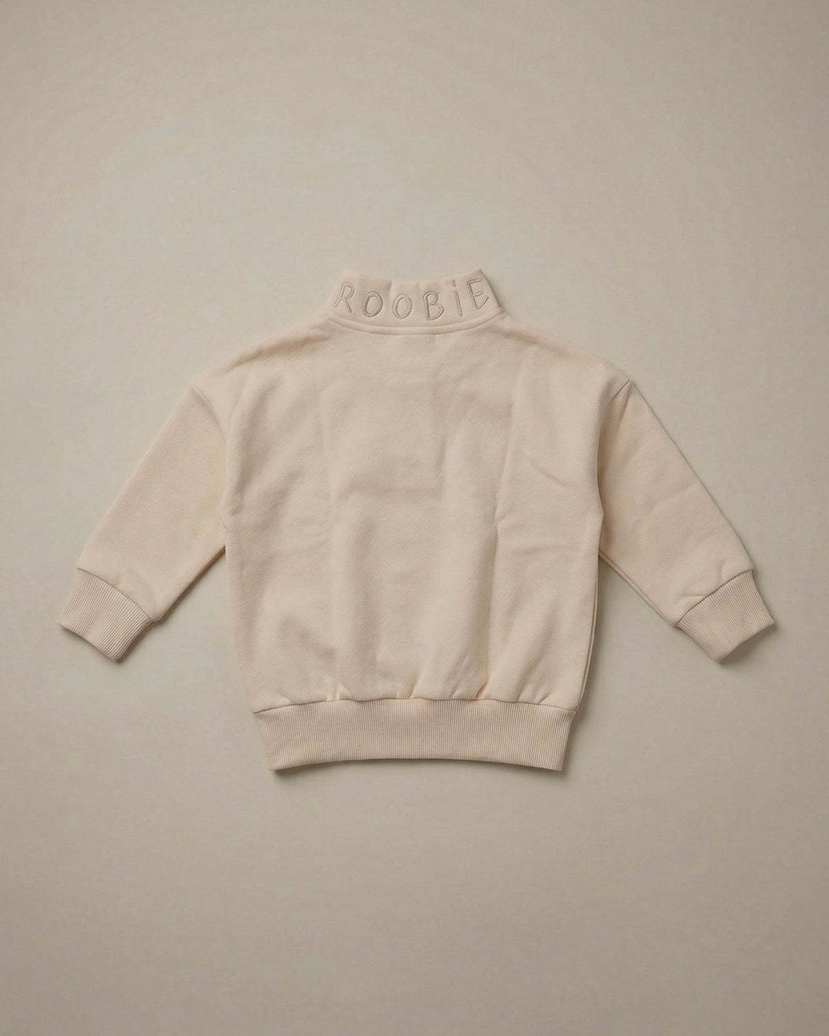 Cream quarter-zip sweatshirt by ROOBiE, designed with oversized fit, shown as a simple product flat lay.