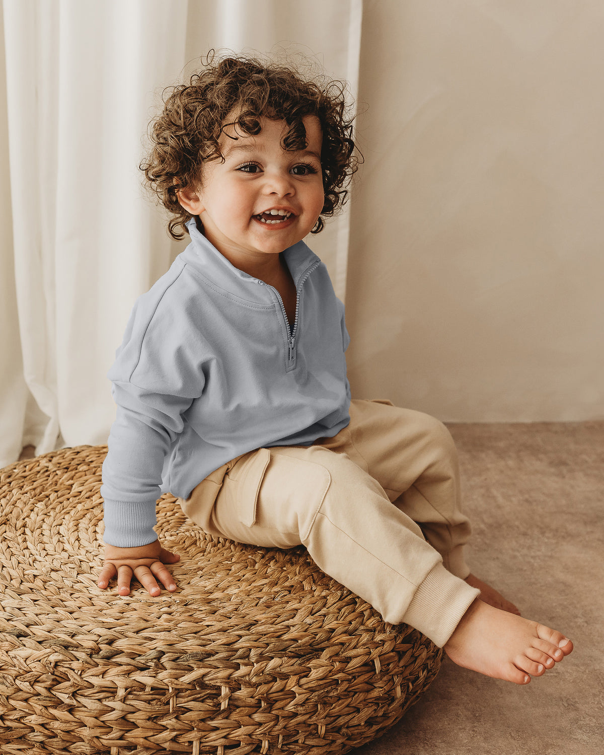 A toddler boy wearing light blue quarter-zip sweatshirt from ROOBiE, featuring quarter-zip neckline and oversized fit, photographed against a neutral background.