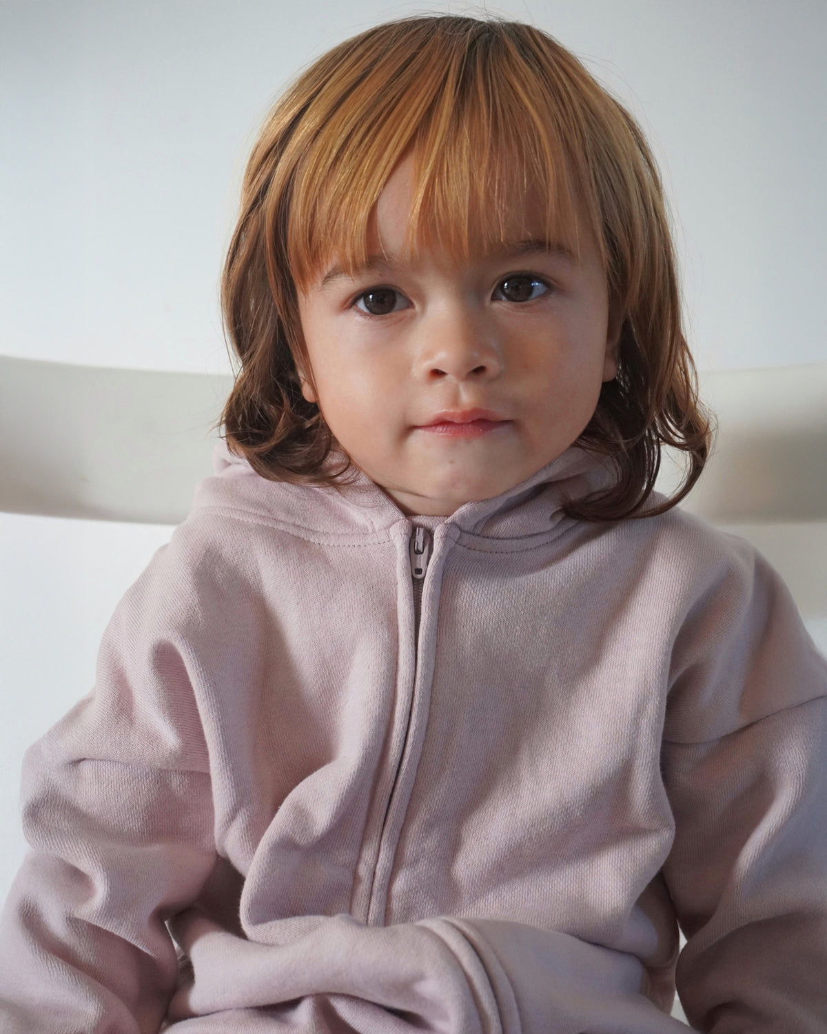 Child wearing a light pink hooded one-piece with a neutral background